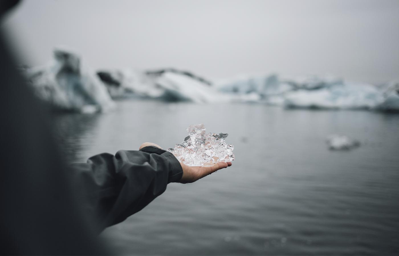A person wearing a spray jacket holding ice in their hand in front of a lake